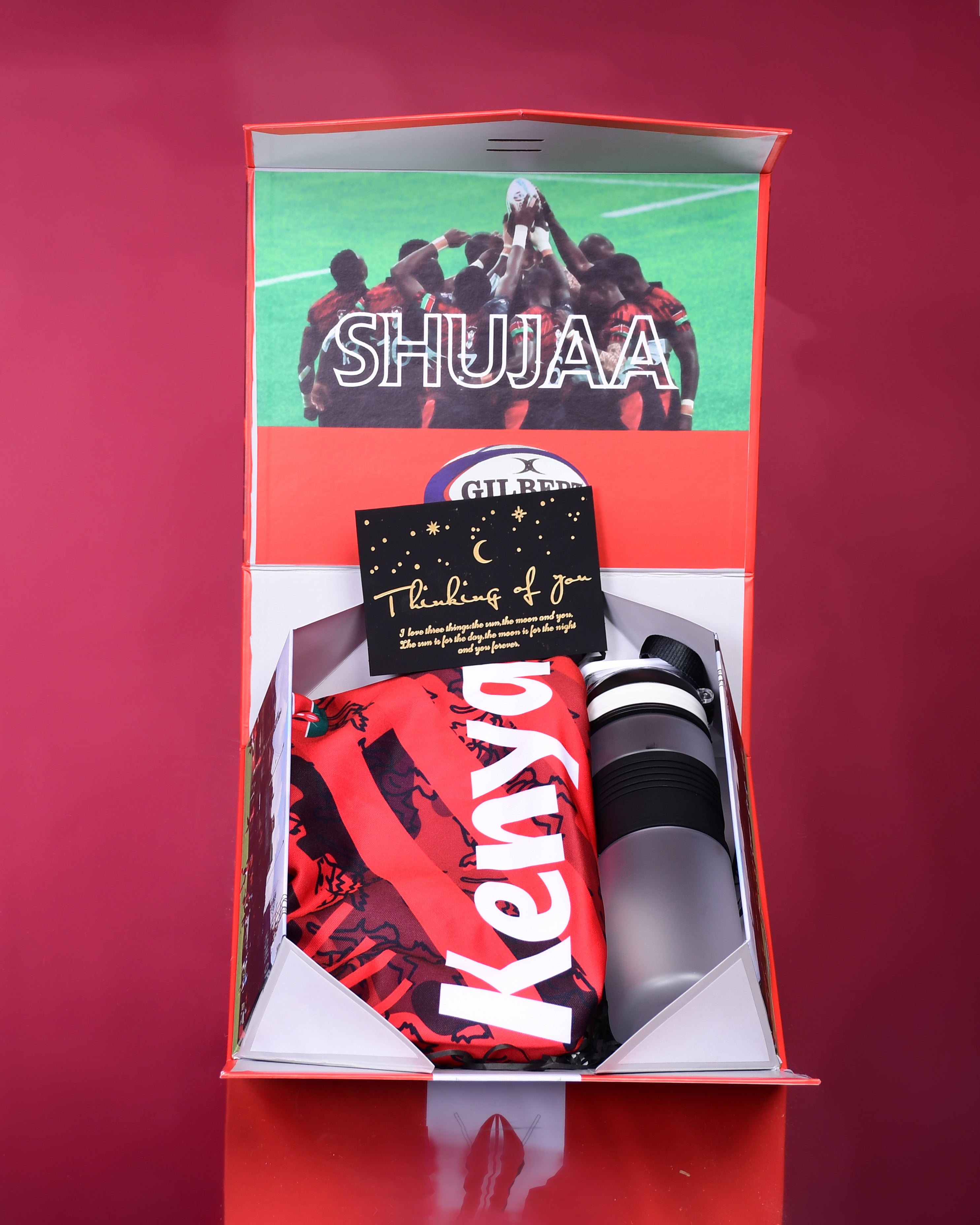 Gift set with a red and black item, a card, and a bottle in a box labeled 'SHUJAA'.